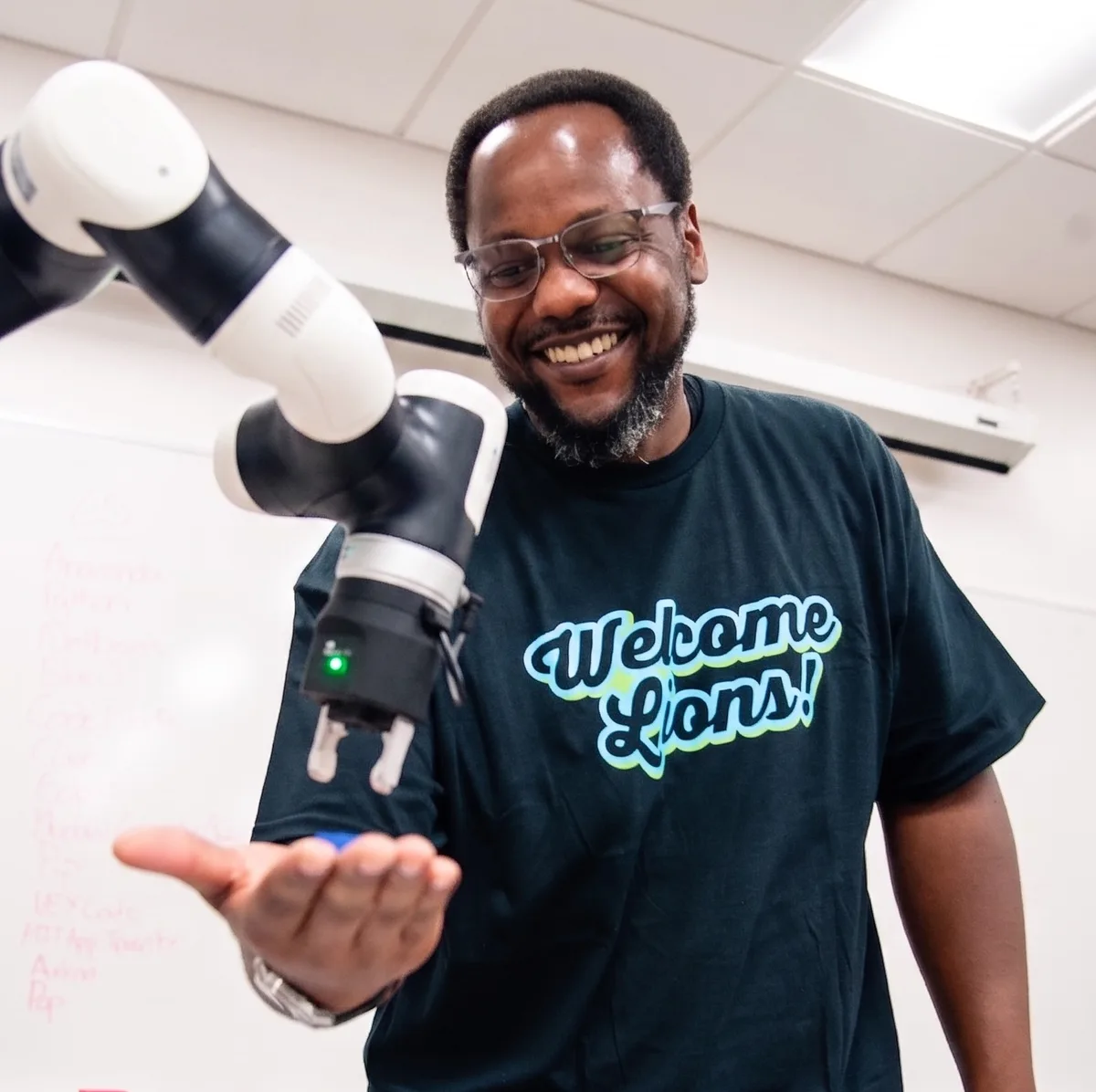 A smiling person beside an industrial robotic arm in a lab