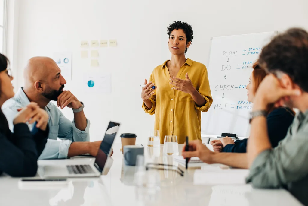 A leader presenting to colleagues at a conference table in front of a whiteboard